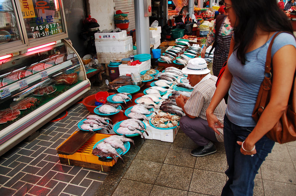 A woman looks at fish and crabs laid out on plastic trays by a vendor at an outdoor market in Gyeongju, South Korea photo_0
